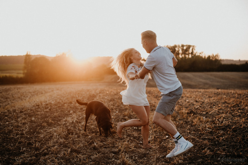 Paarfotoshooting in Kiel auf einem Feld im Sonnenuntergang mit Hund